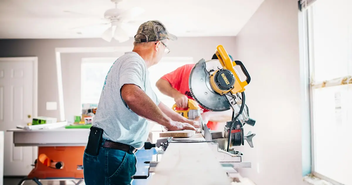 A contractor cutting trim at a miter saw inside a home being remodeled.
