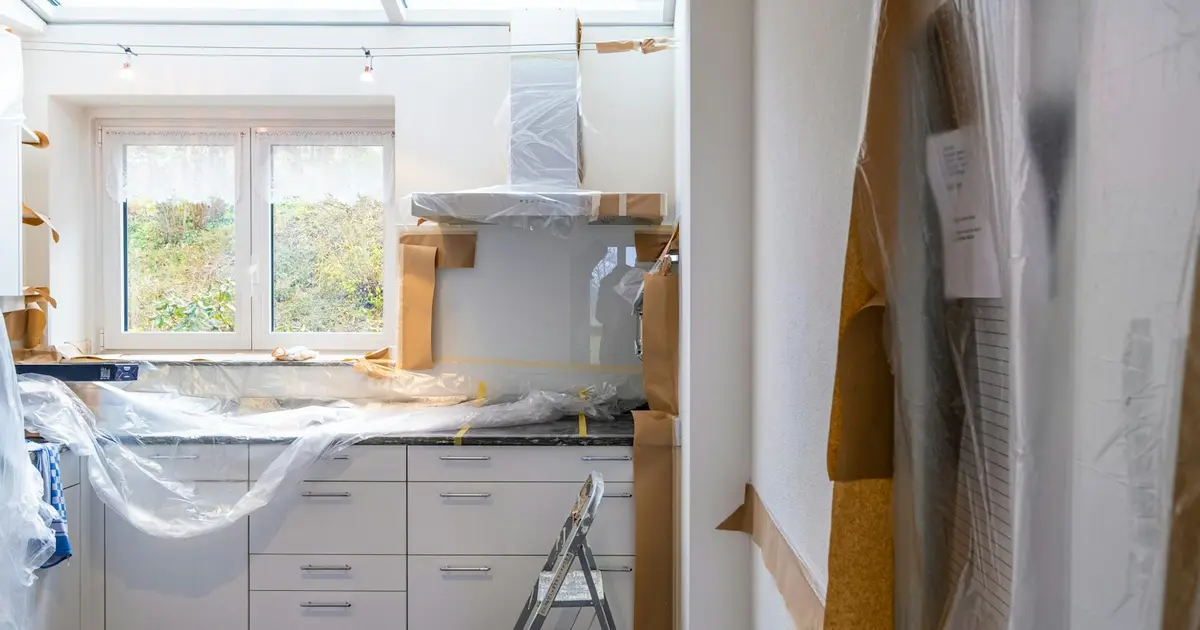 A kitchen in the middle of a renovation, with cabinets covered in plastic.