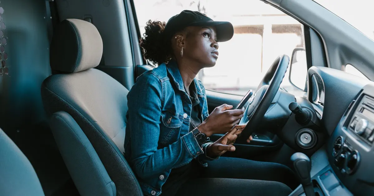 A woman in the driver's seat of a parked car with her phone in hand.