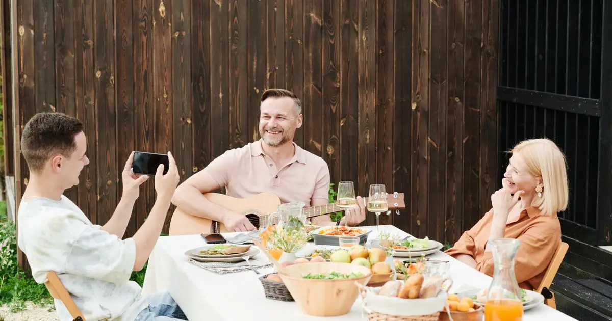 A family laughing together around an outdoor dinner table while the dad plays guitar.