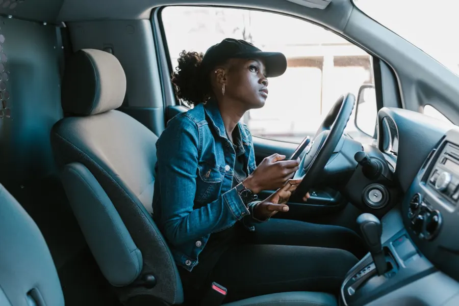 A woman in the driver's seat of her parked car with her phone in hand, between stops.